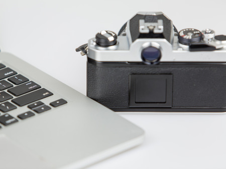 vintage camera and a laptop on a white table with white background. film camera out of foucs.