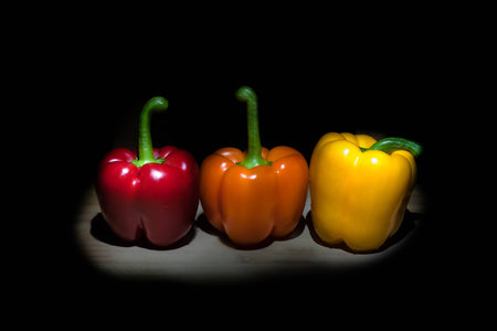 Red orange and yellow bell peppers in the spotlight on a dark stage.の写真素材