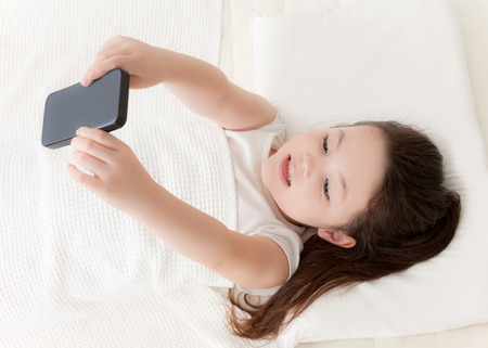 A young girl is spending time in bed playing with a smartphone.の写真素材