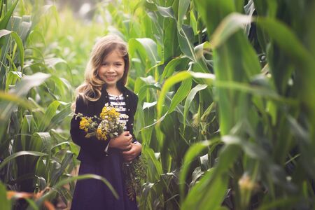 young girl with bouquet of flowers standing in corn field and looking at cameraの写真素材