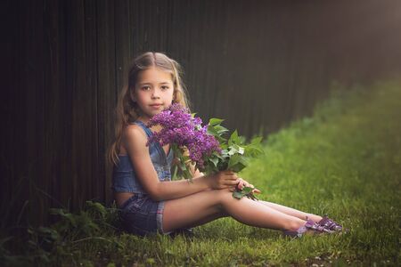 Young girl withlilac in the park, young girl is sitting on the grass with lilac in handsの写真素材