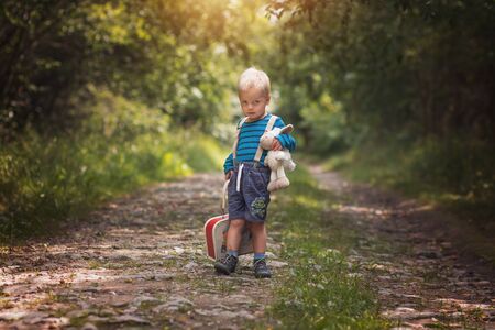 Little boy with plush sheep sitting on the case on the routeの写真素材