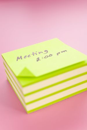 Pile of sticky notes with meeting reminder text over a pink table