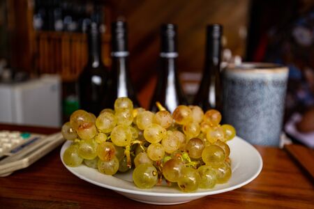 ripe wine grapes on the plate and bottles of wine in vinnery