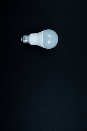 A studio shot of a modern, LED bulb with a screw base, isolated on a textured black background. Represents power, efficiency, and new ideas. Presented in the left center of vertical picture.の写真素材