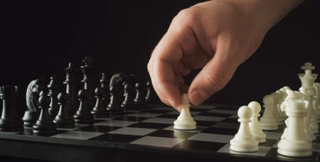 Game of chess. Waiting for the start. Male hand puts a white chess piece pawn on the chessboard on black background. The concept of business strategy, startup, success. Depth of fieldの写真素材