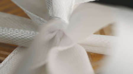 White ribbon bow on yellow gold gift box background. Extreme close-up of a knot. Macro view. Soft...