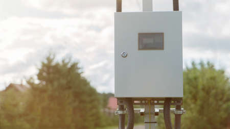 Electrical control box on a street. Outdoor Control switches and electrical switches. Gray hinged power supply on an iron pillar on a clear sunny summer dayの写真素材