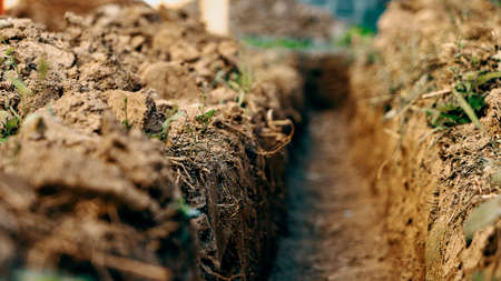 Dig a trench. Earthworks, digging trench. Long earthen trench dug to lay pipe or optical fiber. Construction the sewage and drainage. View from the trench. Clay soil. Part of the image is blurredの写真素材