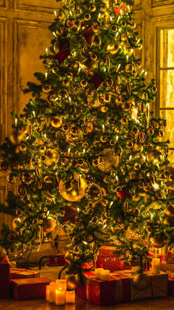Christmas and New Year interior decoration. Green tree decorated with toys, gifts, present boxes, flashing garland, illuminated lamps. Fireplace and xmas tree. Cozy christmas atmosphereの写真素材