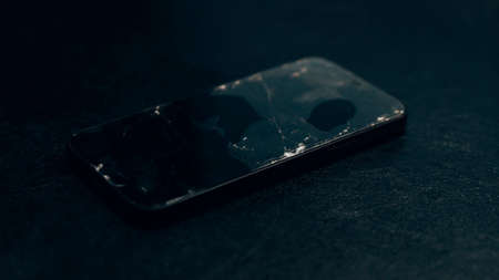 Broken glass screen smartphone on a black textured background. Cracked glass on a screen. Crash phone, fractured, smartphone repair, regret concept. Selective focus, close upの写真素材