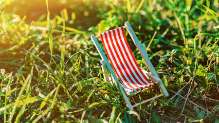Tiny colorful toy deck chair in grass. Summer vacation concept. Sunset time. Children dreaming of holiday rest. Small toy on lawn. springtime and natureの写真素材