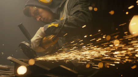 Industrial worker cutting metal with many sharp sparks. Male using special tool for cutting metal at...