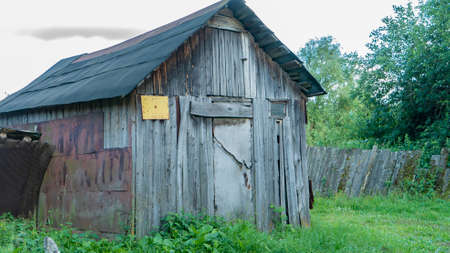 Old wooden shed of weathered boards in country yard on cloudy day. Abandoned farm house in village....