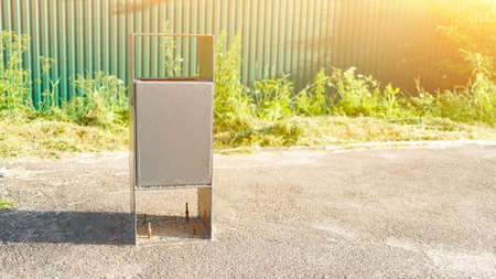 Trash bin and green fence on village street on sunny day. Garbage collecting equipment in public place. Town hygiene service. metal boxの写真素材
