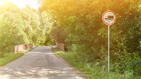 Bridge and Prohibited Lorry road sign in green forest on sunny day. Tranquil country side landscape. Asphalt track and spring nature. empty wayの写真素材