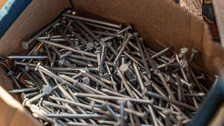 Nails pile in cardboard box close up view. Metal fastening supplies. Construction site materials...