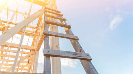 Wooden ladder leaned onto wooden carcass of building at construction site close low angle shot. Traditional equipment and materials. Sunny summer dayの写真素材