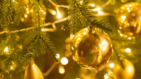 Golden baubles with fairy lights on Christmas tree at home. Holiday ornament with balls and lamp garland on fir tree. Festive decoration with sparkling details and lights on blurry backgroundの写真素材