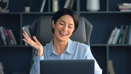 Joyful businesswoman in a modern office, laughing and gesturing during an online meeting, exuding...