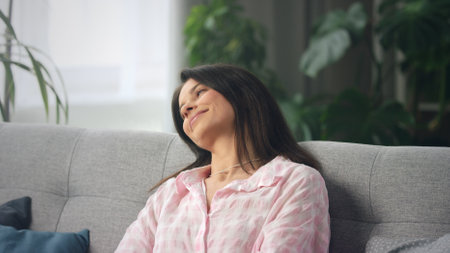 Young woman is spending time at home, sitting comfortably on her couch, with a serene and happy expression on her faceの写真素材