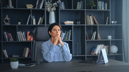 Confident businesswoman at her desk, deep in thought, exuding ambition and leadership in a modern office settingの写真素材