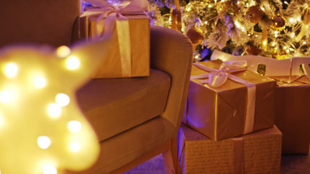 Christmas presents wrapped in gold paper and tied with ribbons are placed under a decorated christmas tree with warm lightsの写真素材