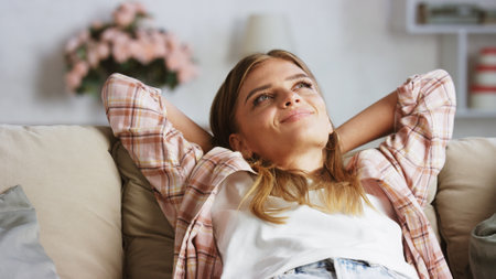 Young woman lying on a comfortable sofa with her hands behind her head, enjoying a moment of peace...