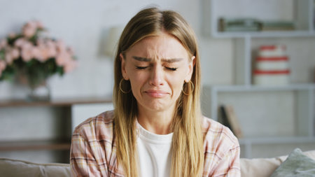 Portrait of a young woman crying on the sofa at home, expressing deep sorrow and emotional distress, grappling with feelings of grief, heartbreak, and lonelinessの写真素材