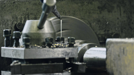 Close up of industrial lathe machine cutting metal part with coolant lubrication, producing metal...