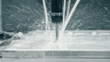 Water cooling system spraying mist over a metal plate while an industrial engraver meticulously engraving intricate designs in a bustling workshop environmentの写真素材