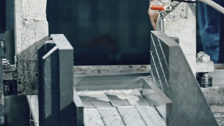 Automated industrial band saw cutting metal profiles with coolant in a metalworking factory, showcasing the precision and efficiency of modern manufacturing processesの写真素材
