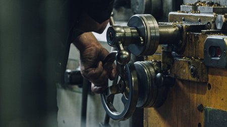 Close up of a metalworker's hands skillfully operating a vintage lathe machine, creating metal parts in a busy workshop environment, showing precision and craftsmanshipの写真素材