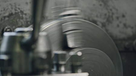 Close up of an industrial lathe machine rotating and shaping a metal piece, showcasing the manufacturing process in a factory setting with blurred foreground elementsの写真素材