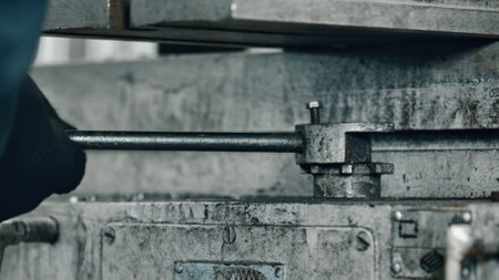 Gloved hand gripping a lever on heavy machinery within a bustling metalworking factory, highlighting the intricate industrial processes and the essence of skilled manual laborの写真素材