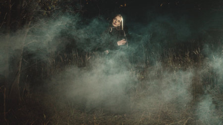 Blonde fashion model posing with arms crossed in a dark, foggy forest at night, enveloped in an air of mystery and creating an evocative, dramatic atmosphere among the treesの写真素材