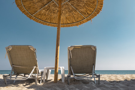 Back view of two lounge relaxation chairs and an umbrella made of straw in front of the horizon line...