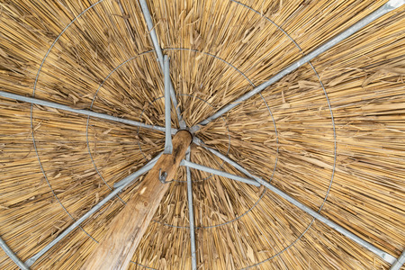 Shot from below of the inside of a tropical beach umbrella made of straw with a wooden and metal structure.の写真素材