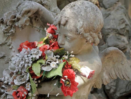 angelic sculpture with flowers , detail of beautiful tomb on monumental cemetery in Italy,...