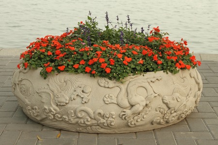 bowl  decorated with dragon reliefs and red impatiens flowers on lake coast in Beihai Parkの写真素材
