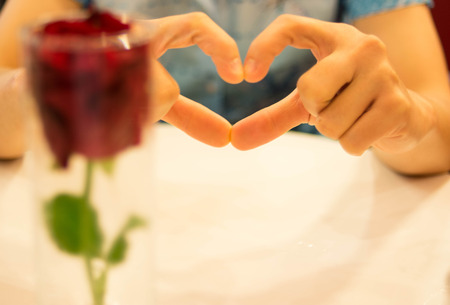 heart symbol by fingers with red rose in glassの写真素材