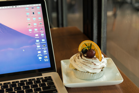 Cake "Banoffe" with caramel and banana place next to laptop in coffee shopの写真素材