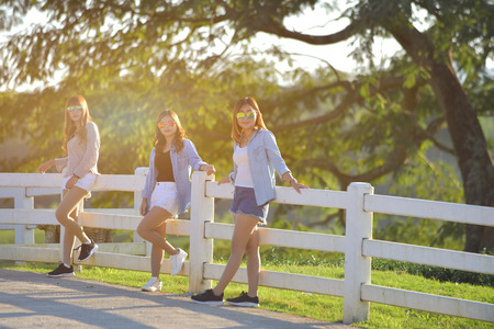 Three beautiful asian girl standing on fence outdoor warm tone. friendship concept in her life style.の写真素材