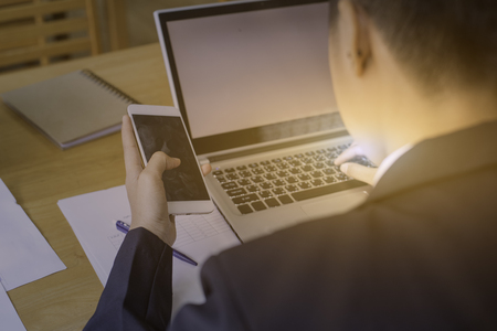 Side view shot of a man's hands using smart phone in interior, rear view of business man hands busy using cell phone at office desk, young male student typing on phone sitting at wooden table, flareの写真素材