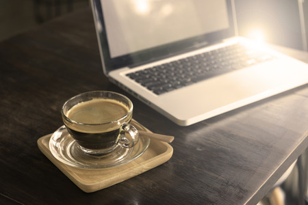 Cup of clear glass hot black coffee on wooden table beside laptop,freelance working space concpet.の写真素材