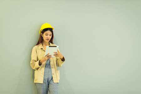 Successful of female Industrial Engineer asian woman in the hard hat uses tablet smartphone computer while Standing against gray wall in the Heavy Industry Manufacturing Factory.の写真素材