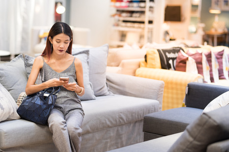 Asian lady sit on sofa and use smart mobile phone to communicate social media and chat after finish...