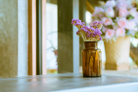 Brown glass bottle with dried pink and purple flower on table in a retro vintage cafe with white and wooden panel backgroundの写真素材