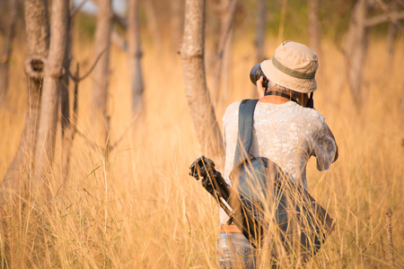 Back side of photographer man in grey grass field with camera on hand.の写真素材