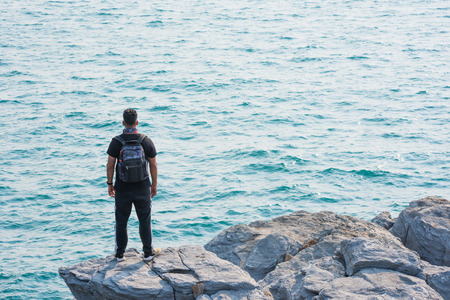 One man with backpack standing by rock at sea.の写真素材